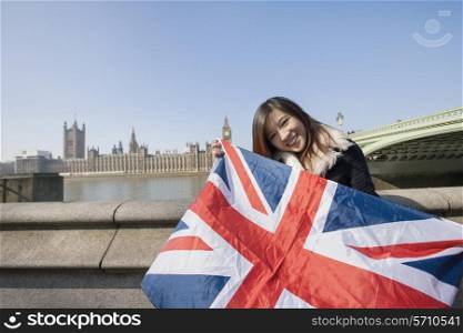 Portrait of happy woman holding British flag against Big Ben at London; England; UK