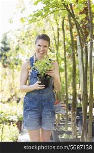 Portrait of happy woman holding potted plant at garden