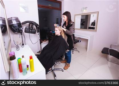 Portrait of happy woman in beauty salon. Blond girl with hair curlers rollers by hairdresser. Hairstyle.