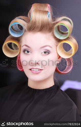 Portrait of happy woman in beauty salon. Blond girl with hair curlers rollers by hairdresser. Hairstyle.