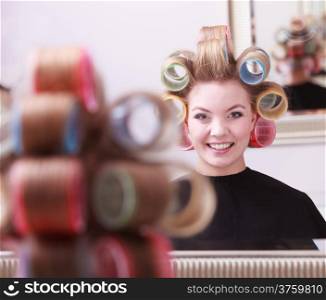 Portrait of happy woman in beauty salon. Cheerful blond girl with hair curlers rollers by hairdresser. Hairstyle.