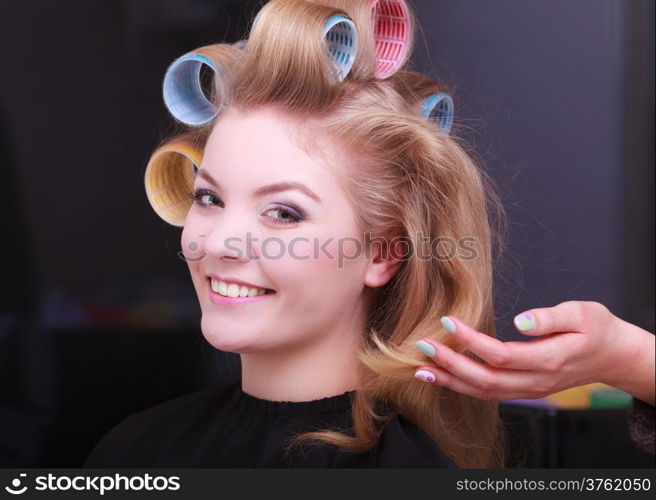 Portrait of happy woman in beauty salon. Smiling blond girl with hair curlers rollers by hairdresser. Hairstyle.