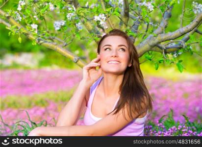 Portrait of happy woman in blooming garden, having fun outdoors, sitting down on pink floral meadow, spring time concept