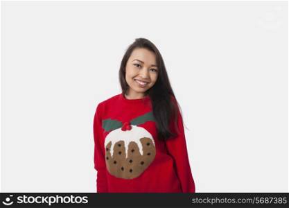 Portrait of happy woman in Christmas sweater standing against gray background