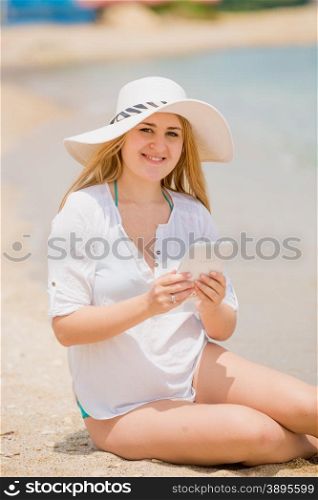 Portrait of happy woman in hat posing with digital tablet on beach