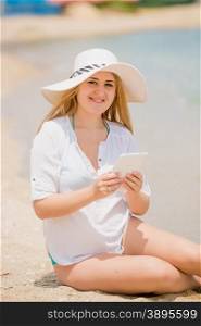 Portrait of happy woman in hat posing with digital tablet on beach