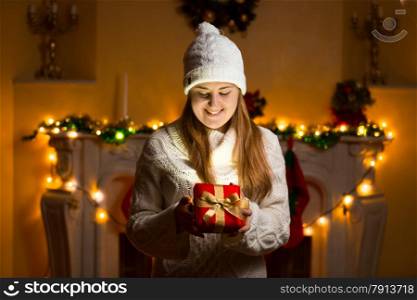 Portrait of happy woman in sweater holding glowing gift box at Christmas eve