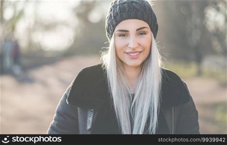 Portrait of happy woman in warm clothing on winter day outdoors. Cheerful girl wearing wool cap and black jacket. Winter and happiness concept. Female person in cold weather.