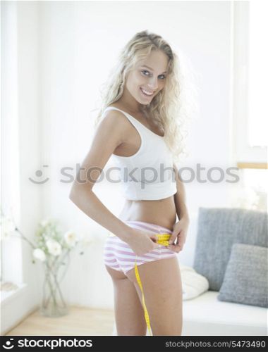 Portrait of happy woman measuring hips with tape