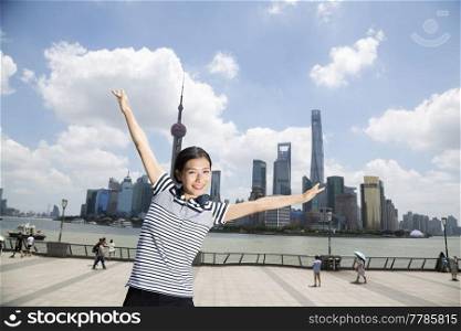 Portrait of happy woman standing with arms outstretched on promenade against Pudong skyline