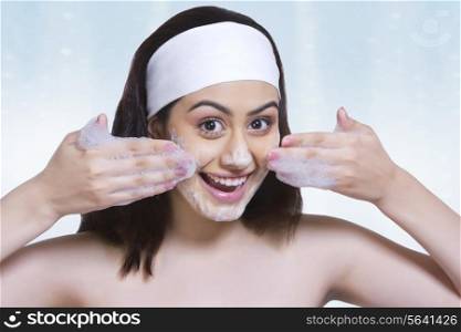 Portrait of happy woman washing face with soap against blue background