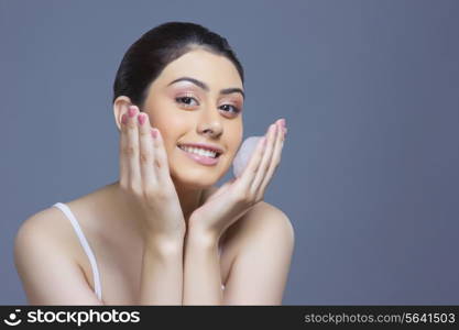 Portrait of happy woman washing face with soap sud against blue background