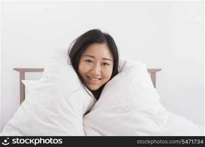 Portrait of happy woman wrapped in quilt on bed