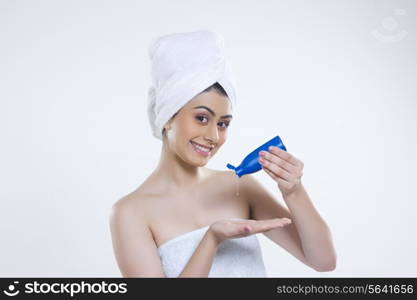 Portrait of happy woman wrapped in towel pouring hair oil on palm against gray background