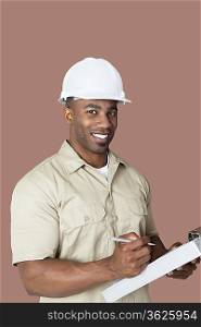 Portrait of happy young African male construction worker holding clipboard over brown background