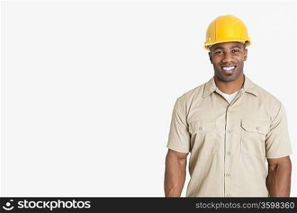 Portrait of happy young African man wearing yellow hard hat helmet over gray background