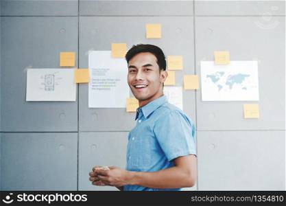 Portrait of Happy Young Asian Businessman in Office Meeting Room. Document&rsquo;s Data Plans and Project as background
