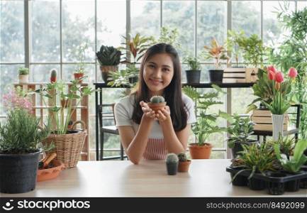 Portrait of happy young Asian female wearing apron uniforms holding her trees and take care of plants while looking at camera at home