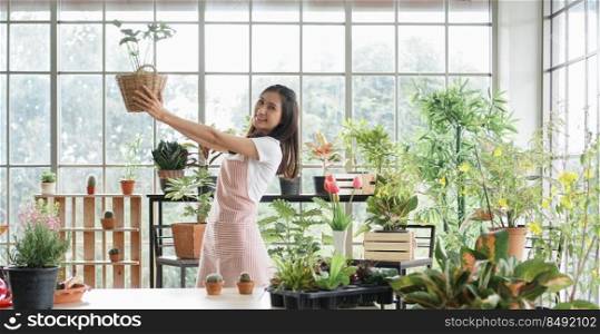 Portrait of happy young Asian female wearing apron uniforms holding her trees and take care of plants while looking at camera at home