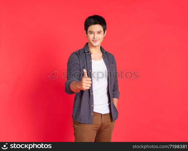 Portrait of happy young asian man dress in casual informal smiling and posing with cheerful and thump up sign isolated on red background.