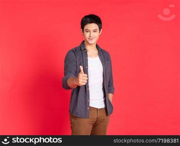 Portrait of happy young asian man dress in casual informal smiling and posing with cheerful and thump up sign isolated on red background.