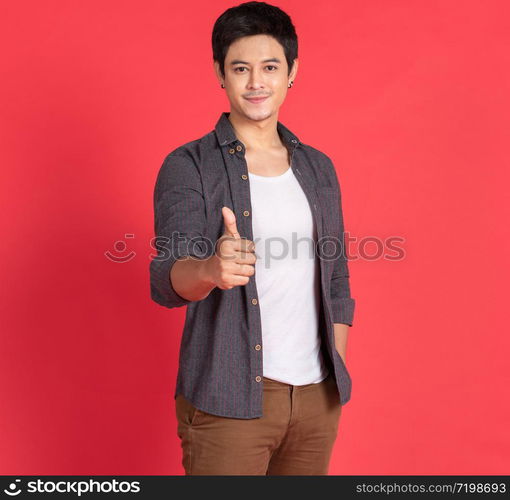 Portrait of happy young asian man dress in casual informal smiling and posing with cheerful and thump up sign isolated on red background.