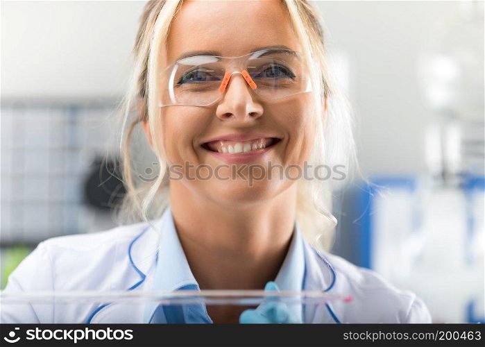 Portrait of happy young attractive smiling woman scientist with protective eyeglasses in the scientific chemical laboratory