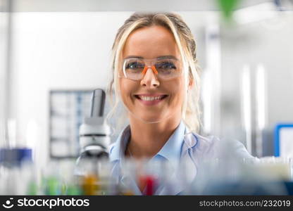 Portrait of happy young attractive smiling woman scientist with protective eyeglasses in the scientific chemical laboratory