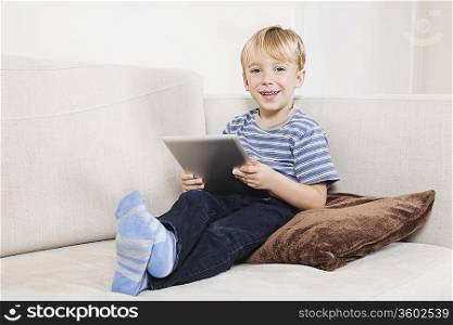 Portrait of happy young boy holding tablet PC on sofa