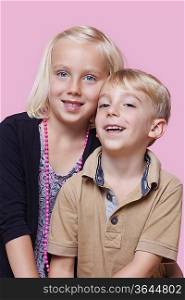 Portrait of happy young boy with sister over pink background