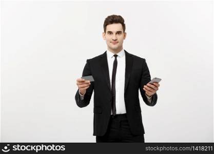Portrait of happy young businessman in smart black suit standing isolated over white wall background. Holding mobile phone and credit card. Portrait of happy young businessman in smart black suit standing isolated over white wall background. Holding mobile phone and credit card.