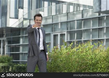 Portrait of happy young businessman pointing at you outside office building
