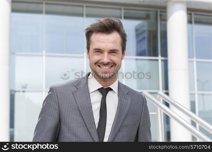 Portrait of happy young businessman standing outside office building