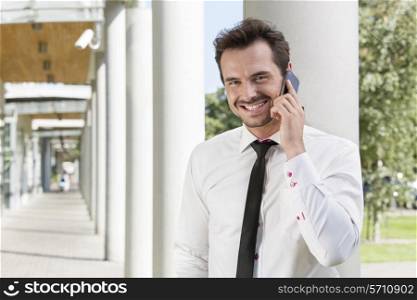 Portrait of happy young businessman using mobile phone outside office