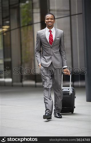 Portrait of happy young businessman walking with wheeled suitcase