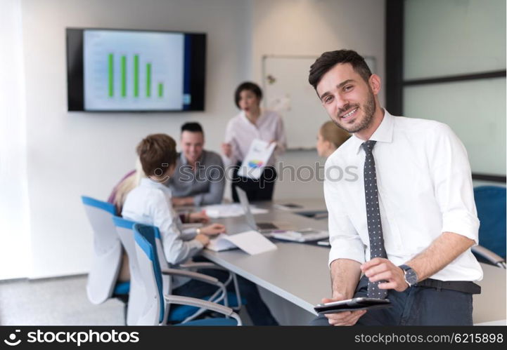 Portrait of happy young businessman with tablet computer office. People group on team meeting in background