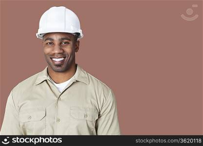 Portrait of happy young construction worker with hardhat over brown background