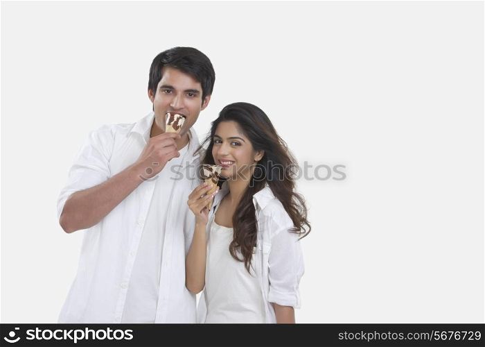 Portrait of happy young couple eating ice-cream cones isolated over white background