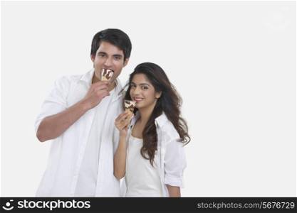 Portrait of happy young couple eating ice-cream cones isolated over white background