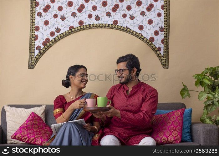 Portrait of happy young couple having coffee while sitting together on sofa at home