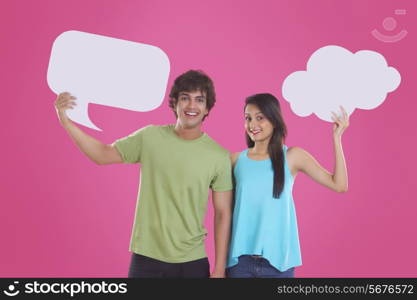 Portrait of happy young couple holding communication bubbles isolated over pink background