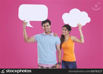 Portrait of happy young couple holding communication bubbles over pink background