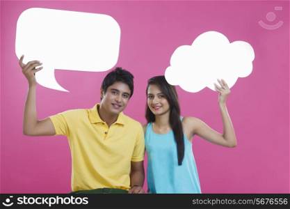 Portrait of happy young couple holding communication bubbles over pink background
