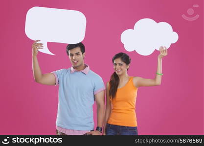 Portrait of happy young couple holding communication bubbles over pink background