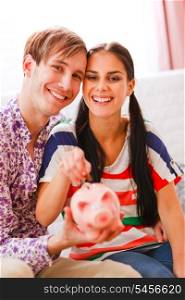 Portrait of happy young couple putting coin in piggy bank&#xA;
