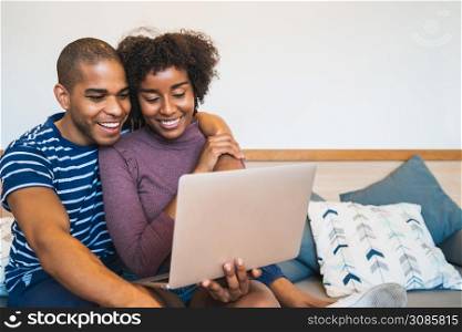 Portrait of happy young couple relaxing and using laptop on couch at home. Lifestyle and relationship concept.