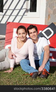 Portrait of happy young couple sitting in front of their new home