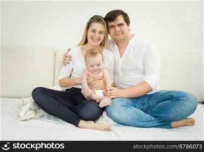 Portrait of happy young family posing with baby son on bed