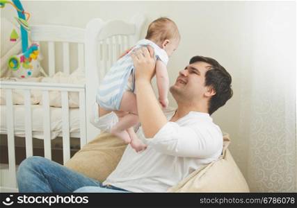 Portrait of happy young father sitting in bag chair and playing with his 6 month son