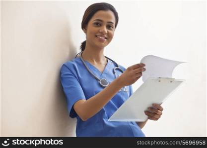 Portrait of happy young female surgeon with clip board against white background